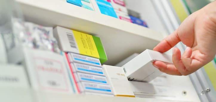 A pharmacy worker packing shelves with medication boxes.