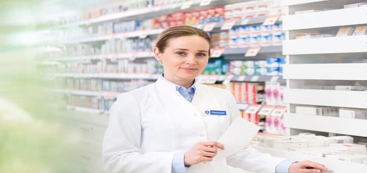 a female pharmacist in a white coat, packing shelves with medication boxes