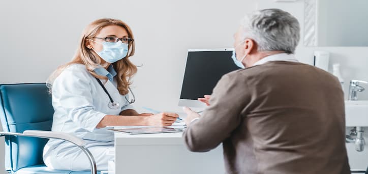 Woman doctor wearing a facemask consulting an elderly patient