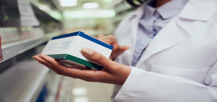 A pharmacy technician stacking medication boxes onto shelves and checking the contents.