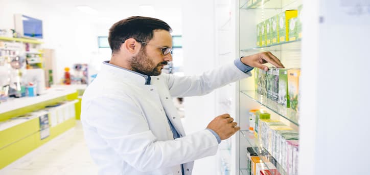 A male pharmacist placing a medication box into the shelves of the pharmacy.